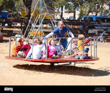 father-pushing-kids-on-a-merry-go-round-at-a-playground-B5H08H.jpg